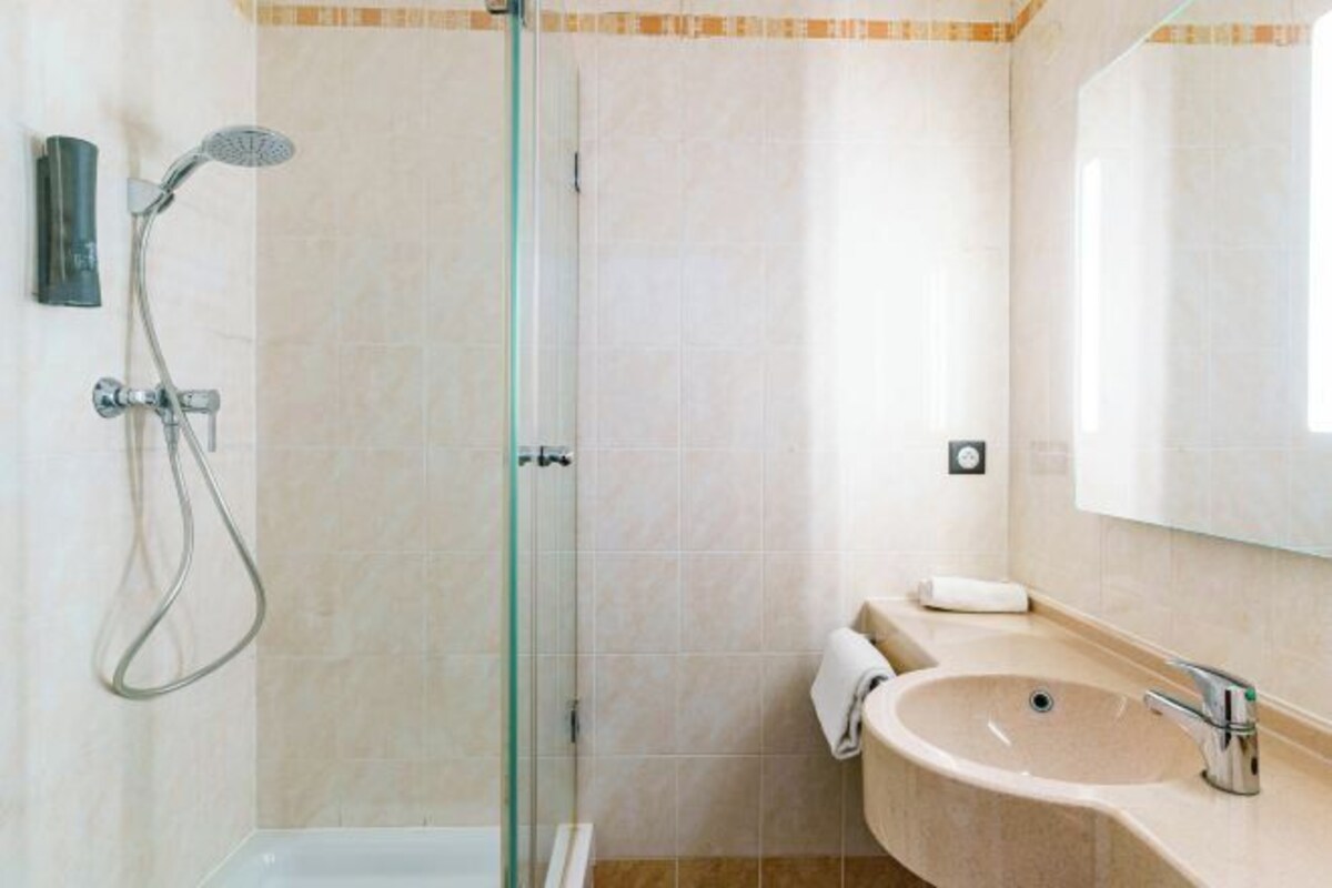 A modern bathroom with a glass-enclosed shower, a beige sink, and a large mirror.