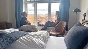 Et hotelværelse med et stort vindue, en seng, en stol og en lampe.