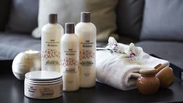 Productos de terapia de spa, como gel de ducha, loción corporal y champú, dispuestos sobre una mesa con velas y toallas.