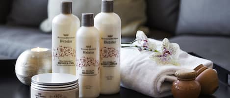 Productos de terapia de spa, como gel de ducha, loción corporal y champú, dispuestos sobre una mesa con velas y toallas.