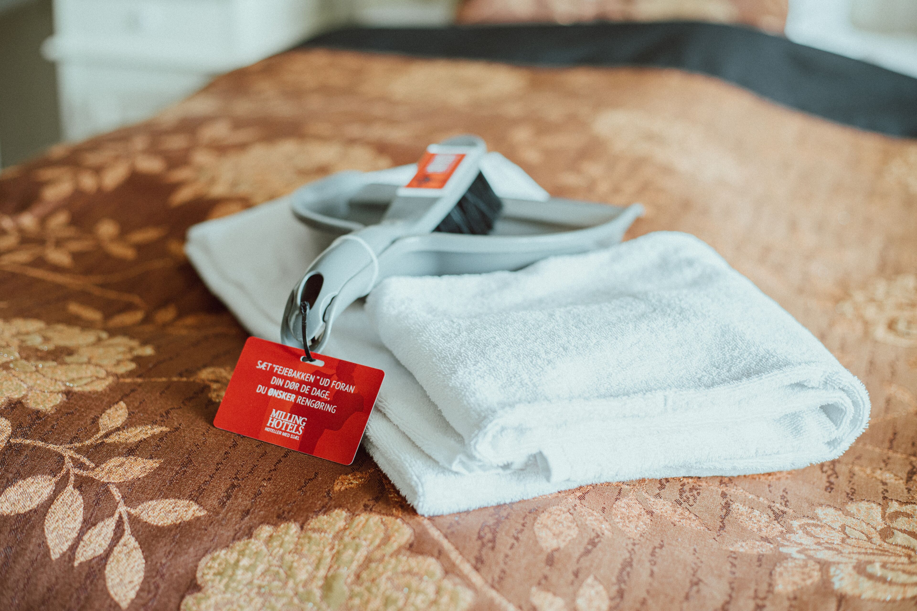 A neatly folded white towel with a tag on a patterned bedspread.