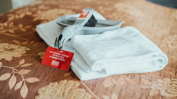 A neatly folded white towel with a tag on a patterned bedspread.