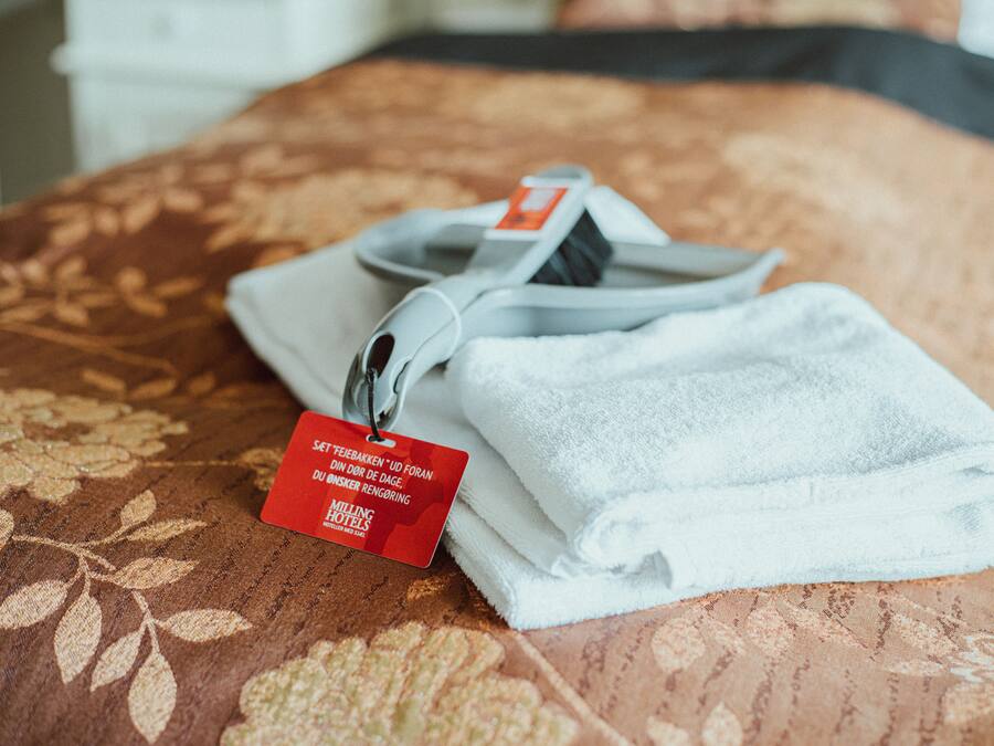 A neatly folded white towel with a tag on a patterned bedspread.