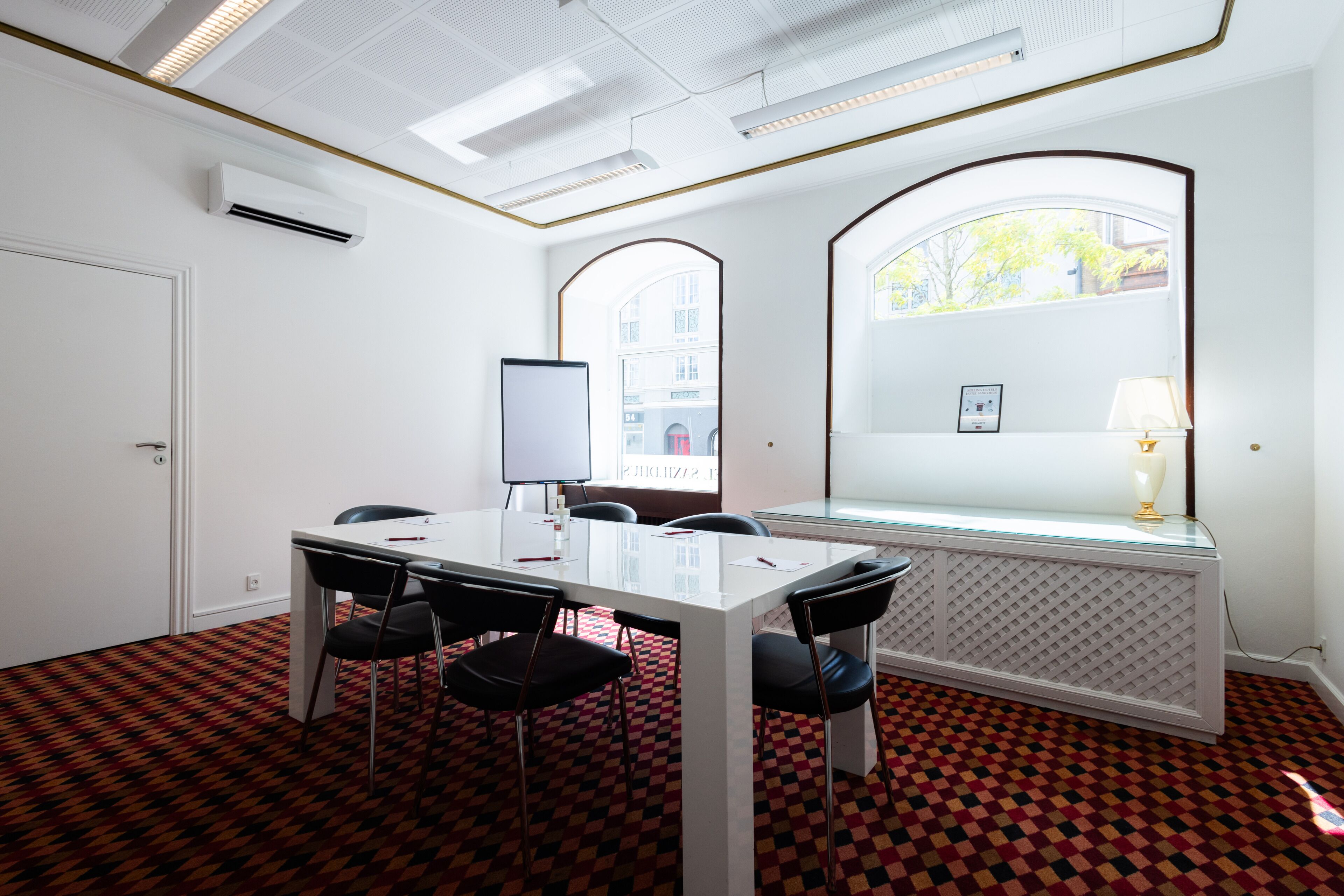 A conference room with a white table, black chairs, a whiteboard, and a window with a view of buildings.