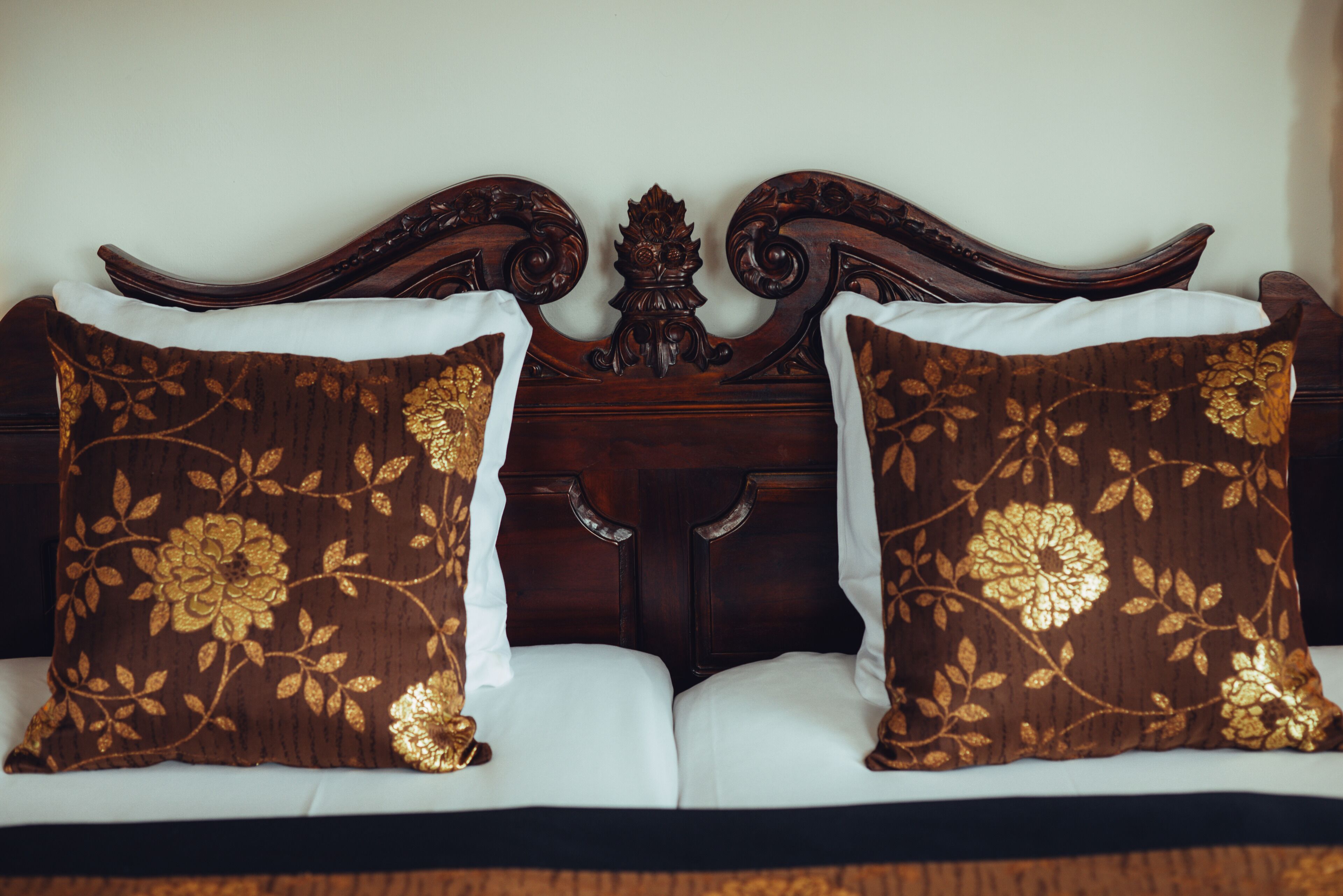 A bed with a dark wooden headboard and two decorative pillows with floral patterns.