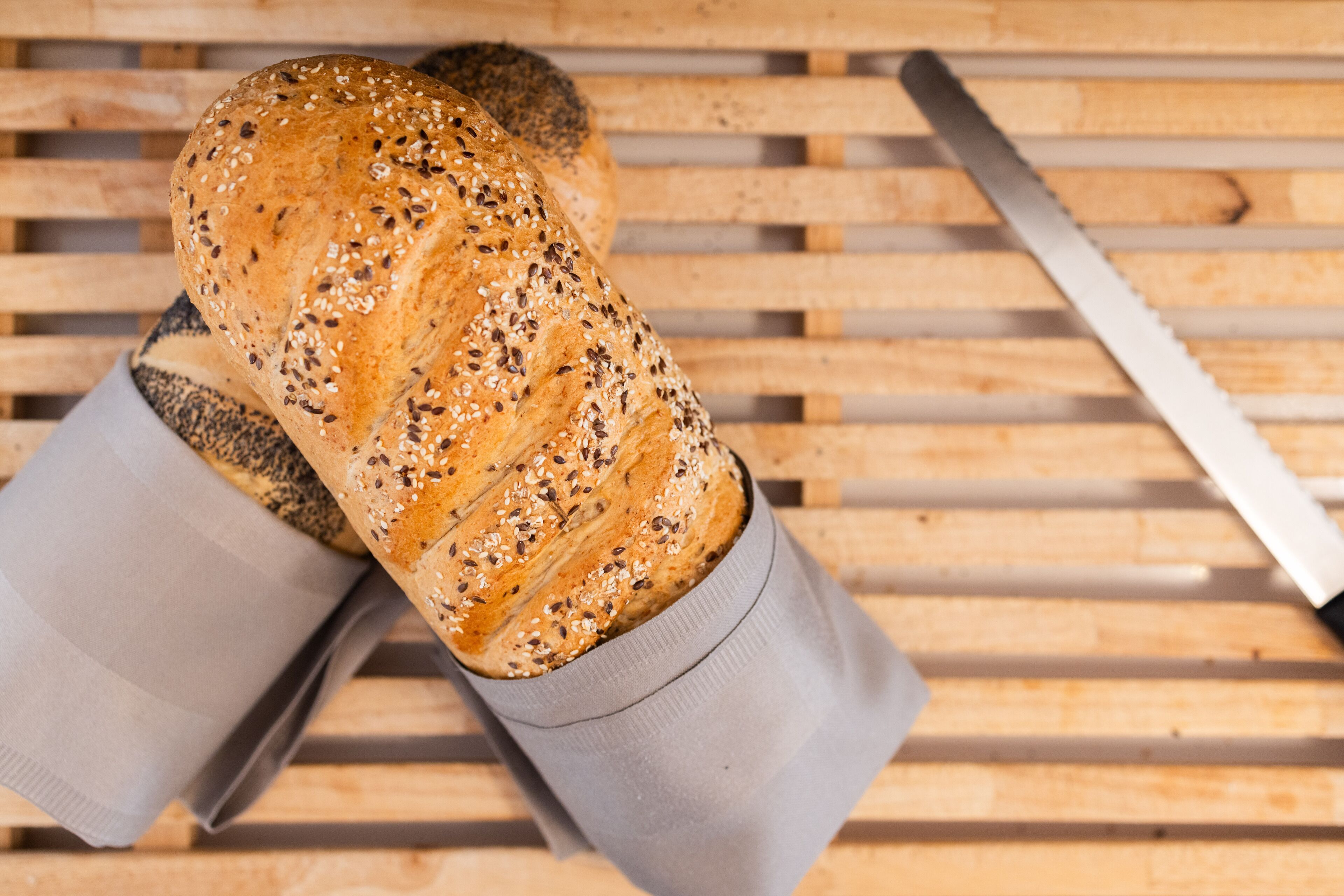 Two loaves of seeded bread on a wooden surface with a knife.