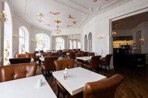 A spacious dining area with high ceilings, chandeliers, and large windows. Tables are arranged in rows with brown leather chairs. - Milling Hotel Saxildhus (Kolding)