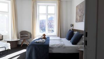 Una habitación de hotel con una cama, una silla, una mesita y una ventana con cortinas.