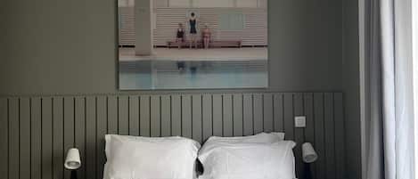 A bedroom with a large bed, two bedside tables, a hanging light fixture, and a painting on the wall.