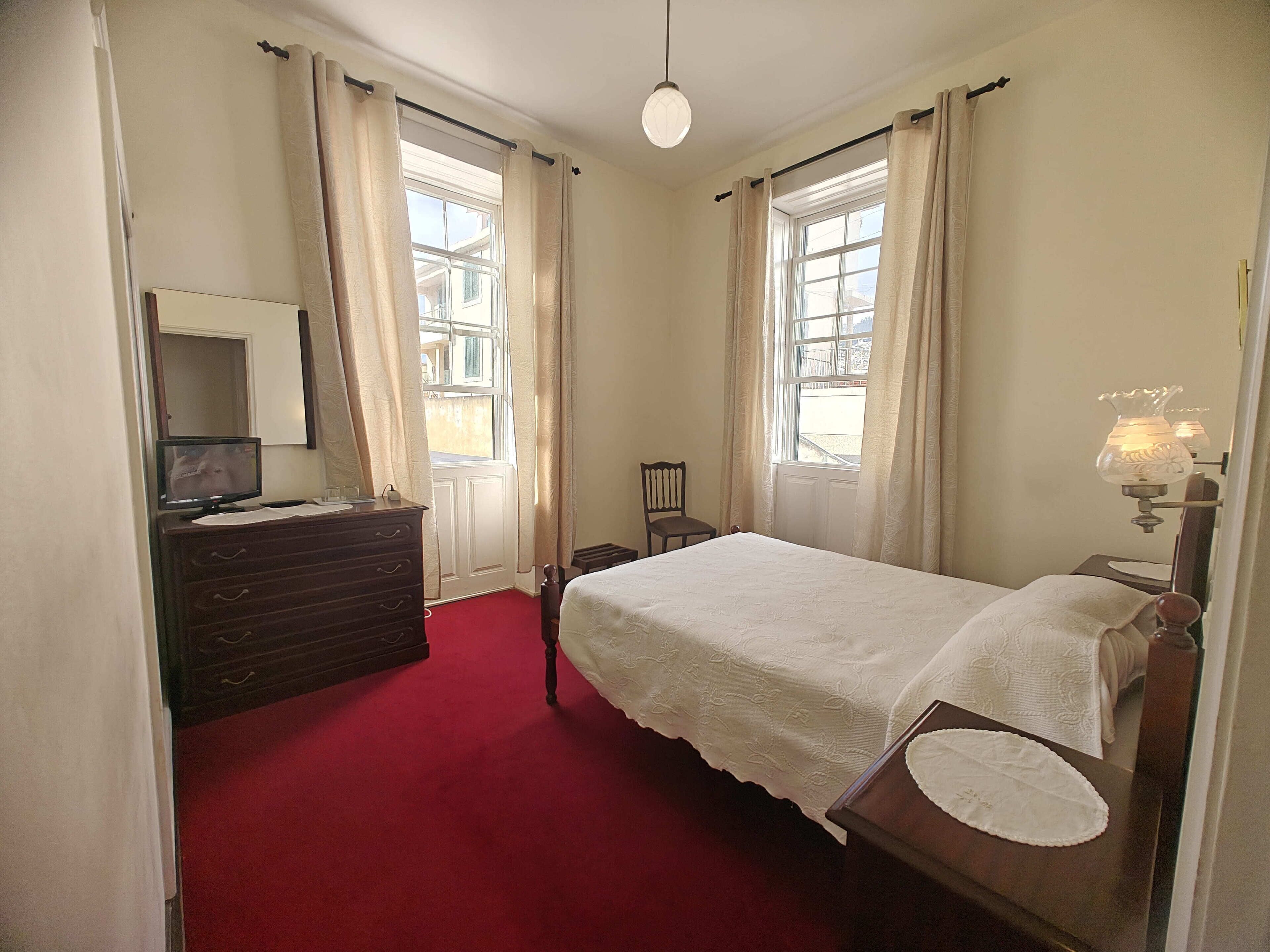 A bedroom with a bed, dresser, mirror, and a television on the dresser.