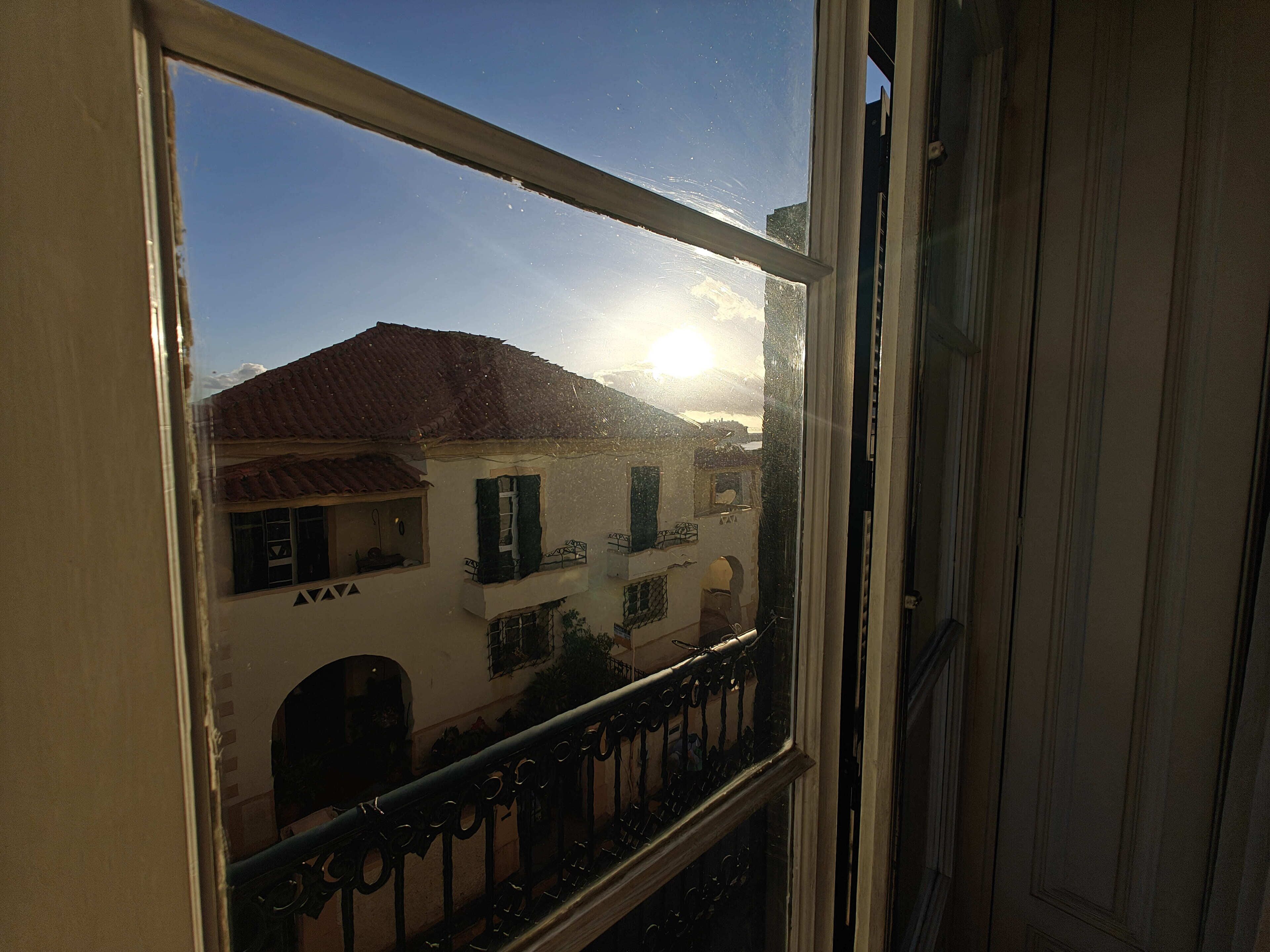 A window with a view of a building with a tiled roof and a balcony with a metal railing.