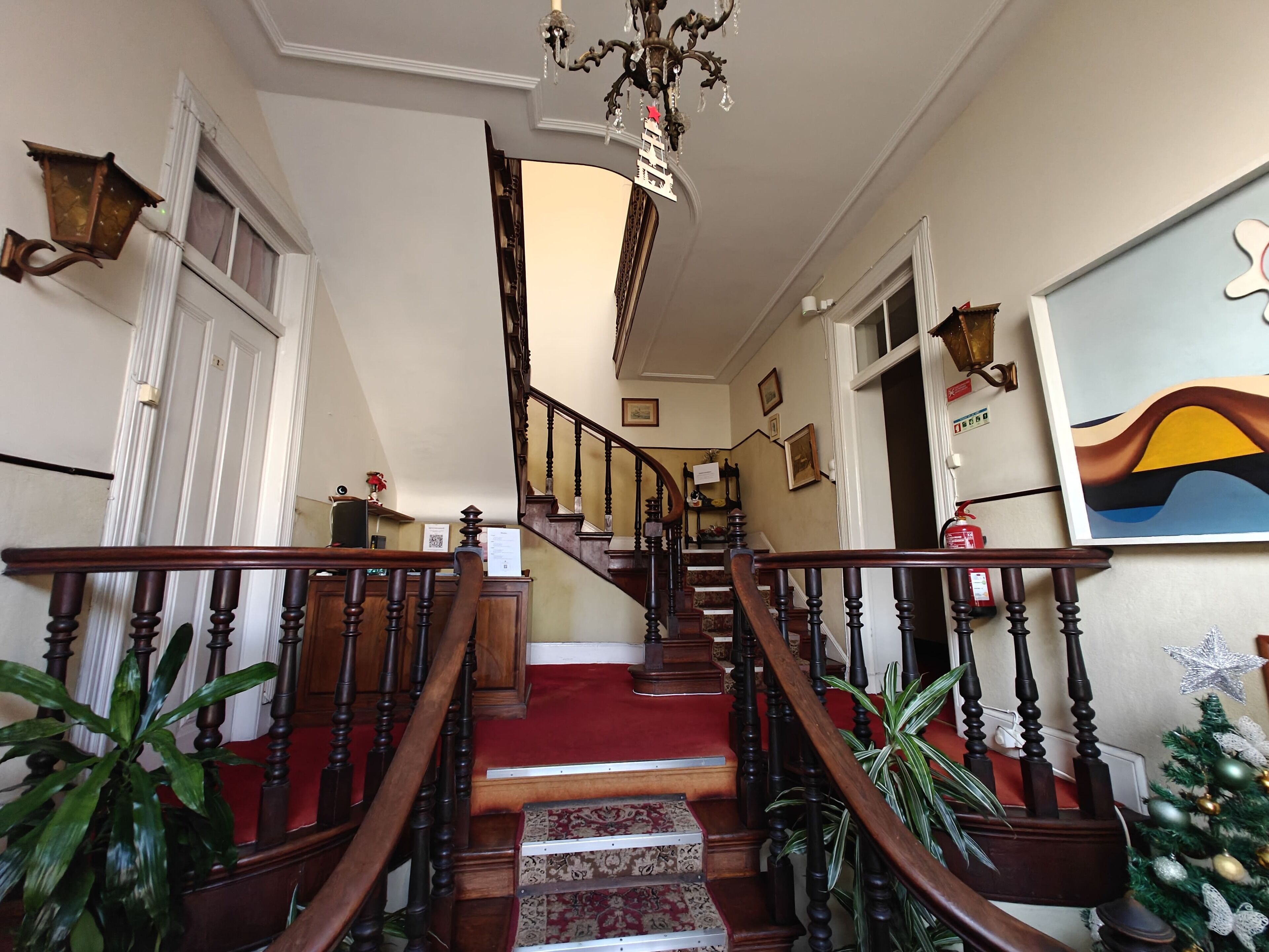 A grand staircase with a red carpet, wooden railings, and a chandelier.