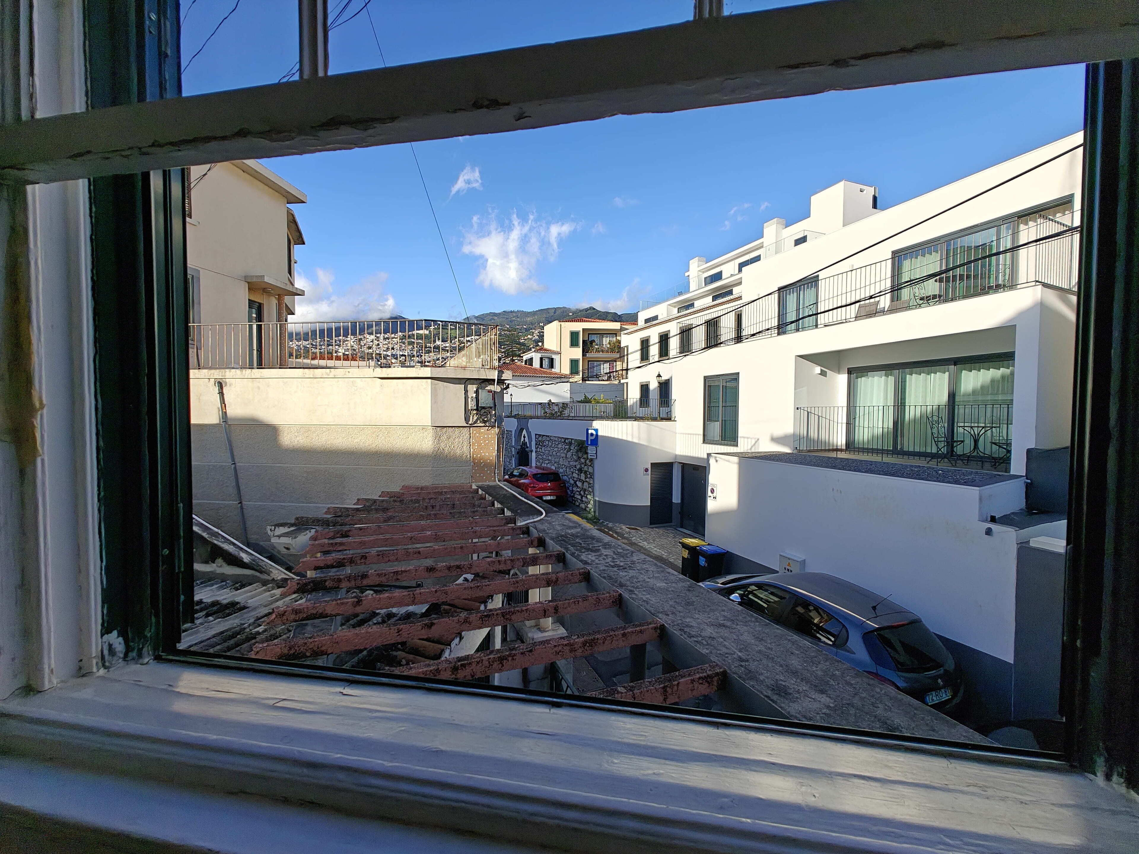Blick durch ein Fenster auf eine Wohnstraße mit einer Treppe, parkenden Autos und Gebäuden mit Balkonen.