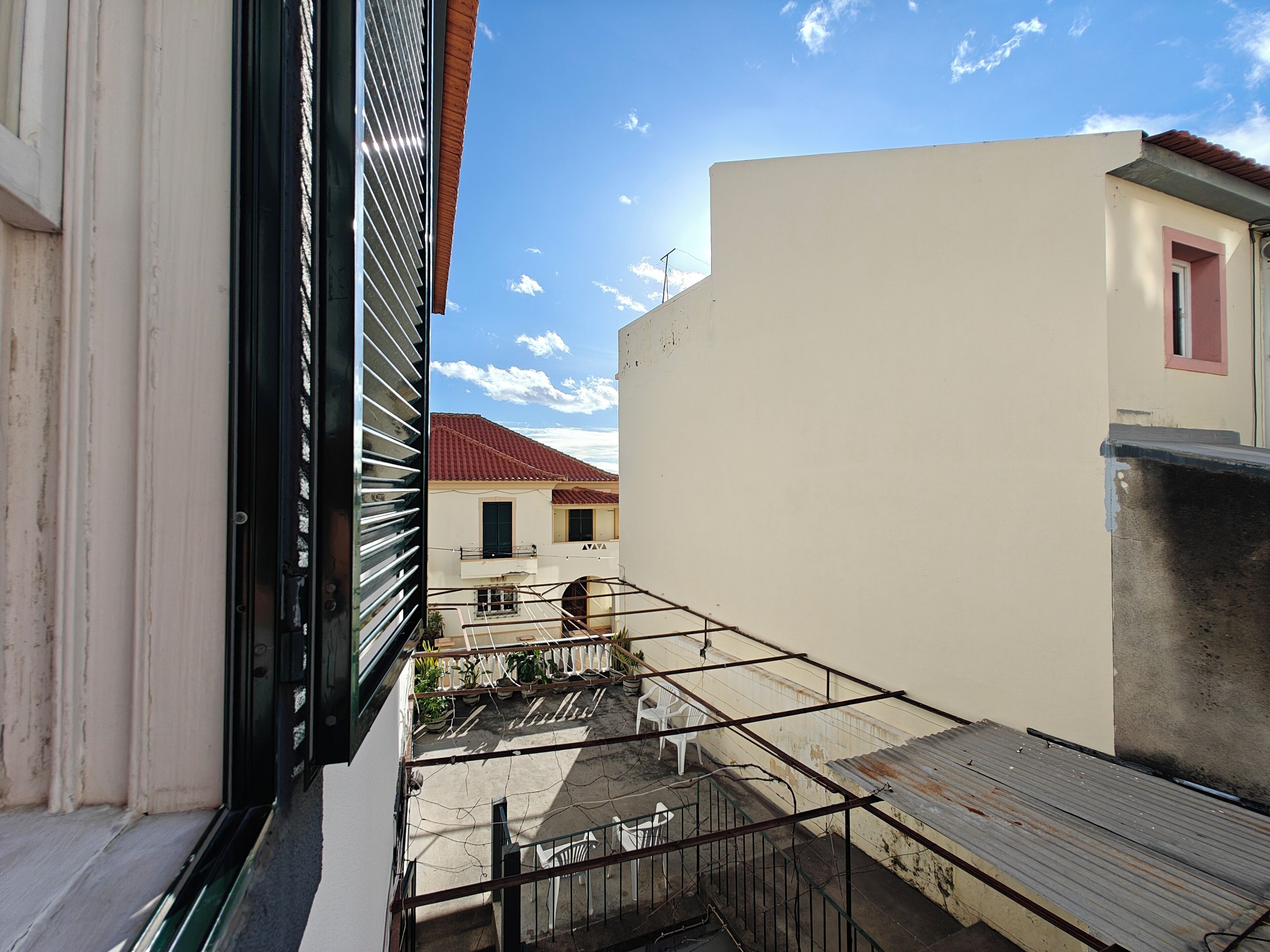 Un balcone con ringhiera in metallo, vista sui palazzi circostanti e cielo sereno.