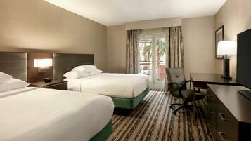 Une chambre d’hôtel avec deux lits, un bureau, une chaise, une télévision et une fenêtre avec des rideaux.
