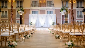 A wedding ceremony aisle with rows of gold chairs and white floral arrangements.