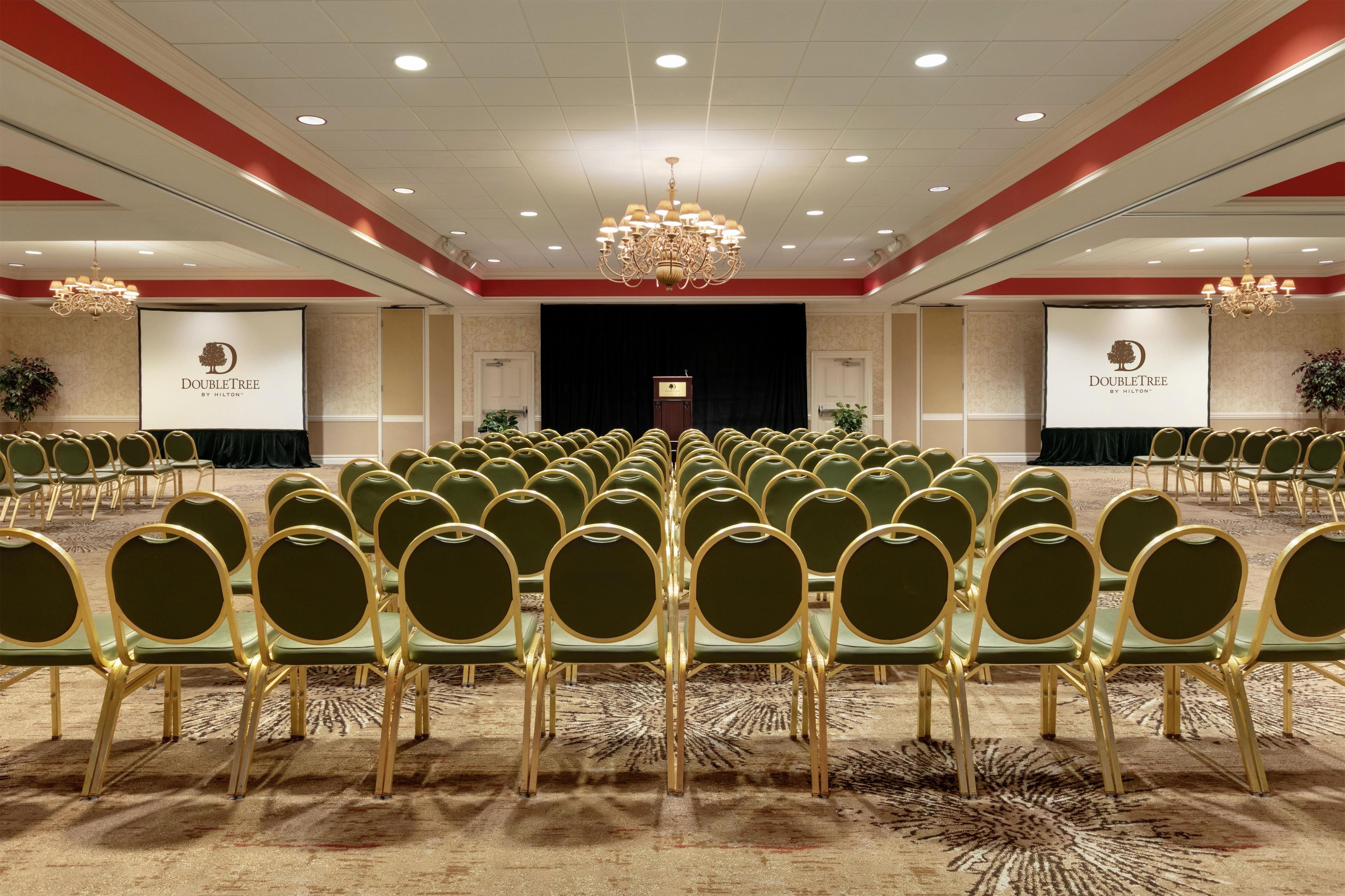 A conference room with rows of green chairs, a stage with a podium, and two banners with the DoubleTree logo.