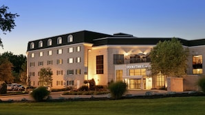 A multi-story hotel with a modern architectural design, featuring a prominent entrance with a sign, landscaped gardens, and a parking area.