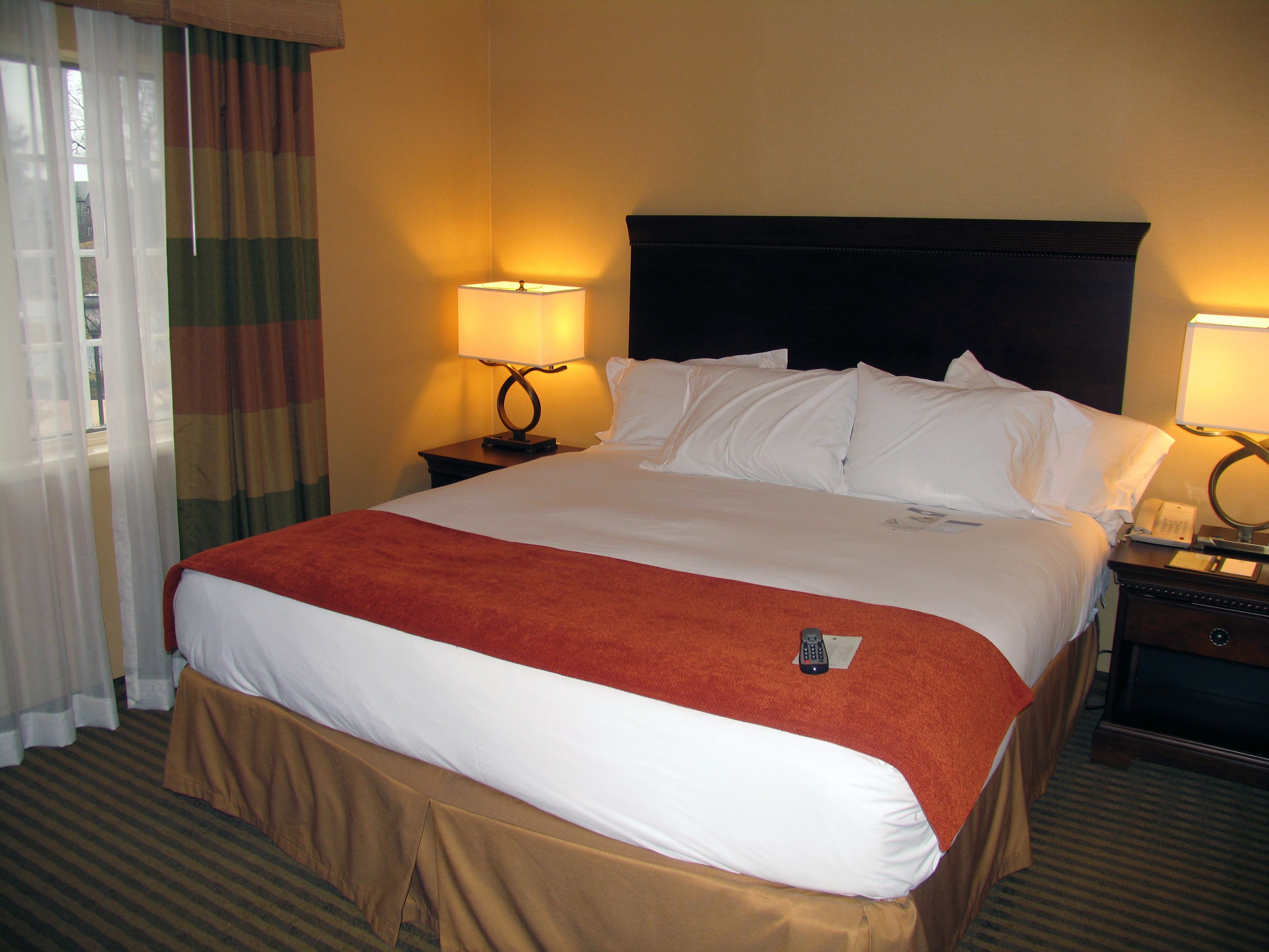 A hotel room with a large bed, two bedside lamps, a telephone, and a window with curtains.