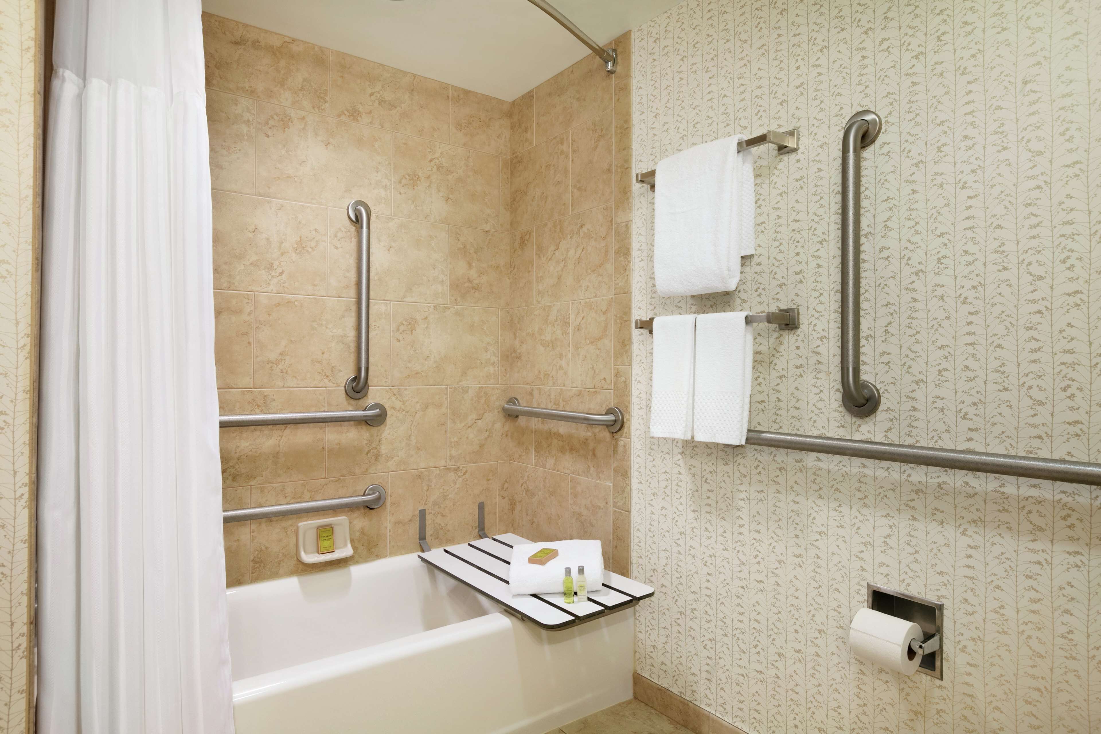 Une salle de bain équipée d’une baignoire, de barres d’appui, d’un porte-serviettes et d’un support à papier toilette.