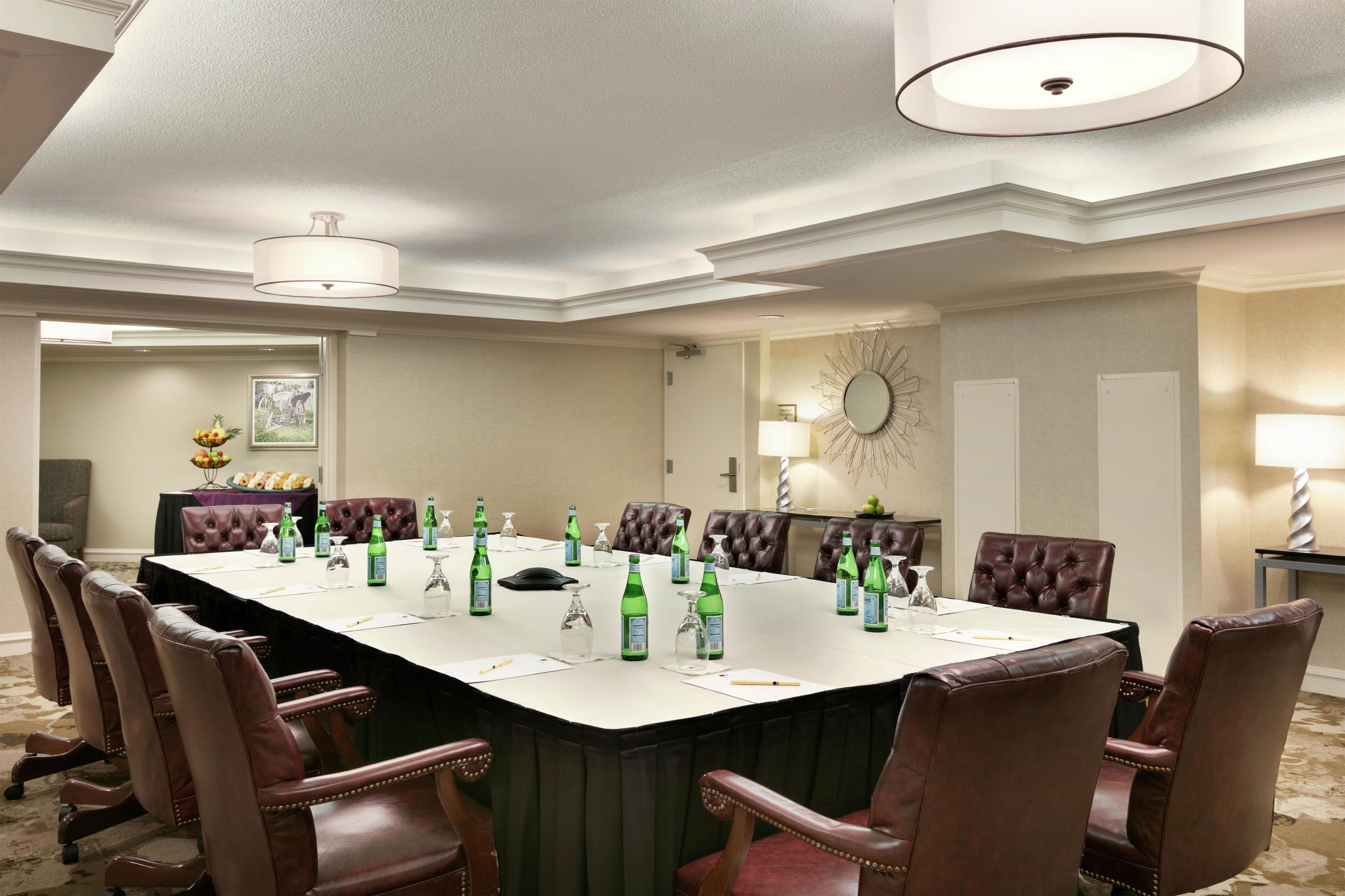 Un salón de conferencias con una larga mesa, sillas y diversos objetos como botellas y vasos.