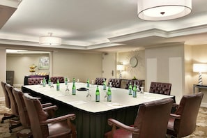 Un salón de conferencias con una larga mesa, sillas y diversos objetos como botellas y vasos.