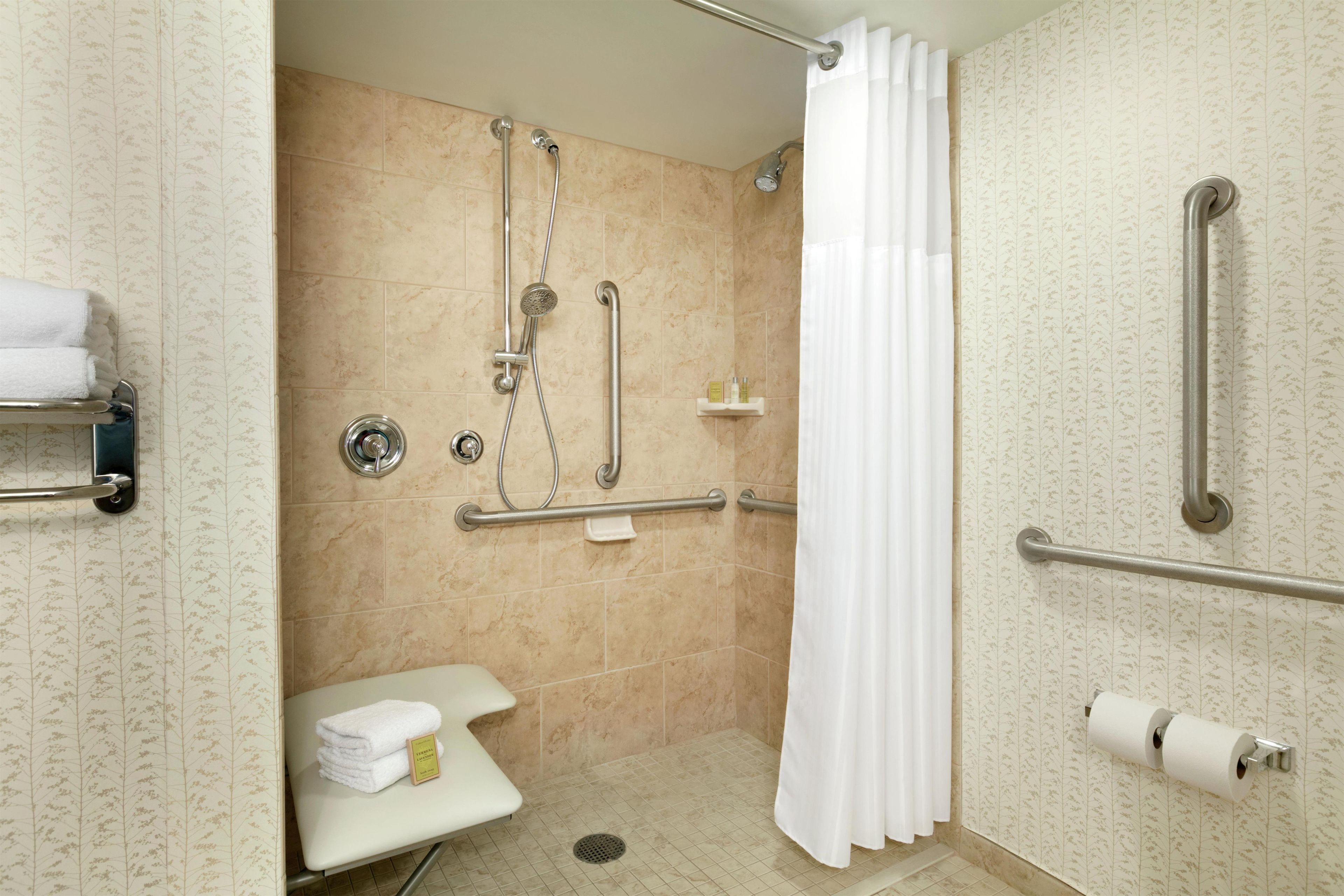 A bathroom with a shower, grab bars, a toilet, a towel rack, and a toilet paper holder.