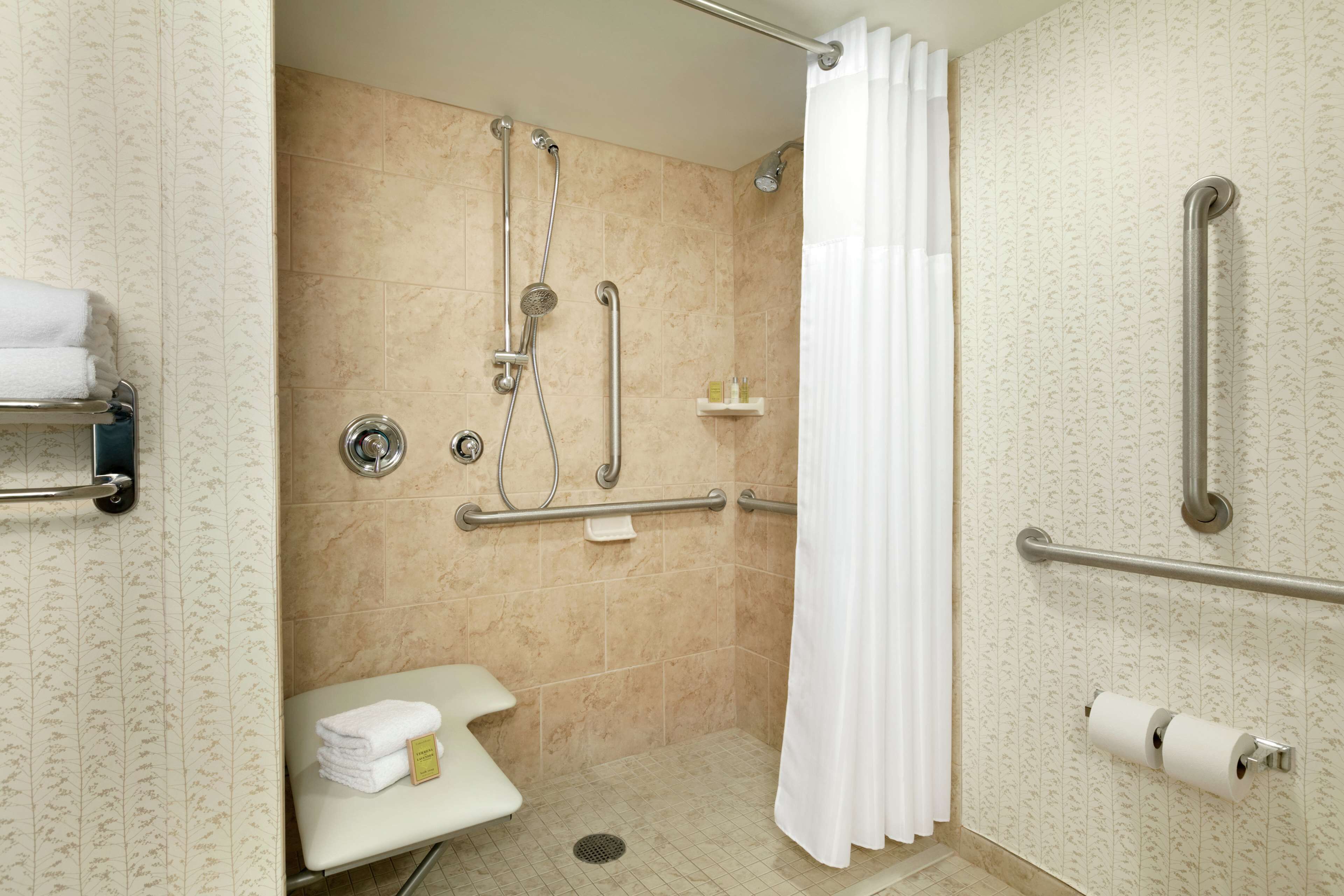 Un baño con ducha, barras de apoyo, inodoro y perchero para toallas.