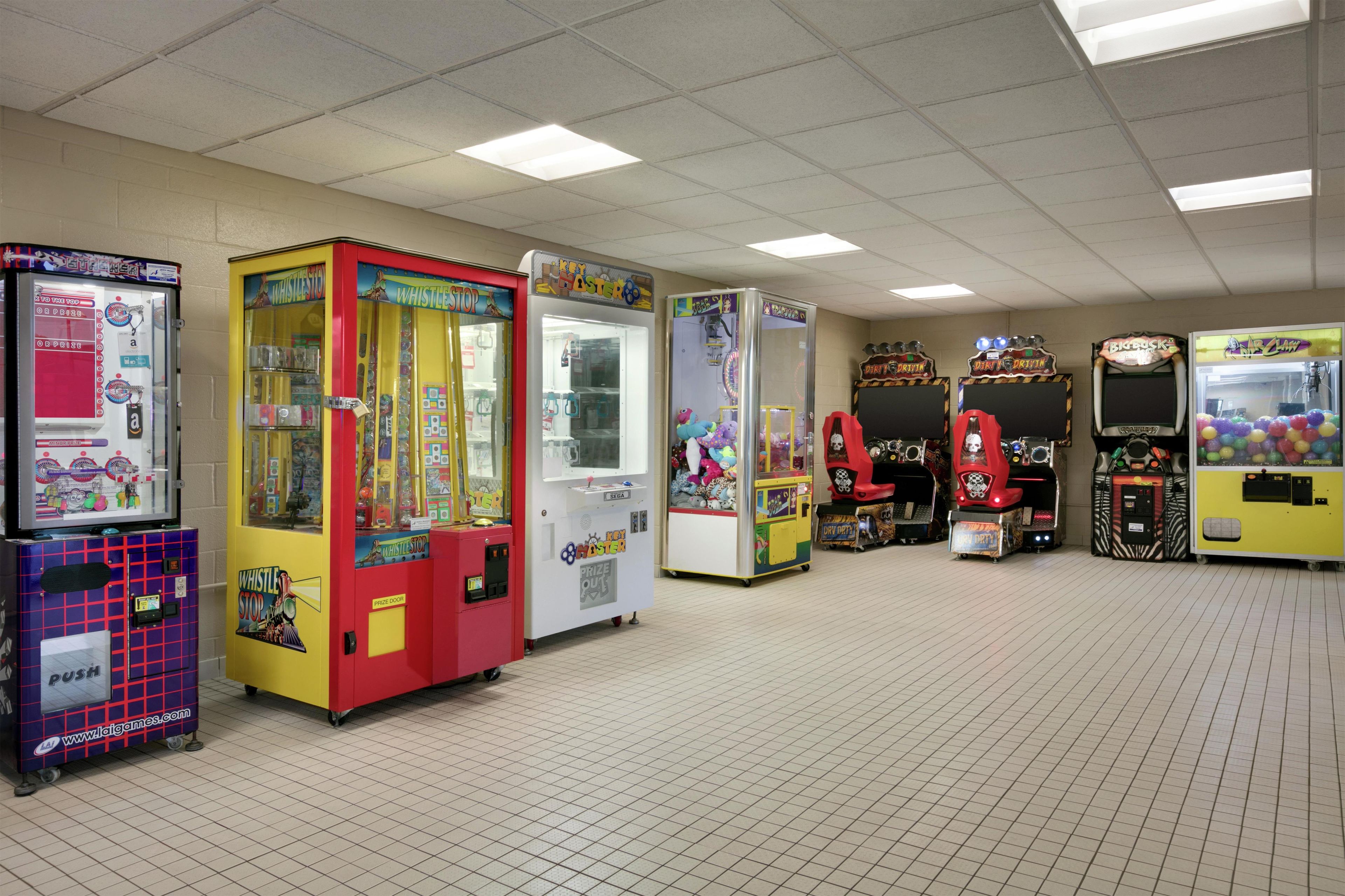 A row of arcade machines in a room with a tiled floor and fluorescent ceiling lights.