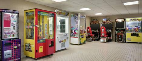 A row of arcade machines in a room with a tiled floor and fluorescent ceiling lights.