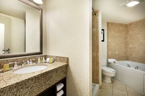A bathroom with a granite countertop sink, a large mirror, a toilet, and a bathtub.
