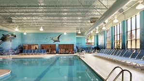 An indoor swimming pool with a dolphin mural, sun loungers, and a clear view of the sky through large windows.