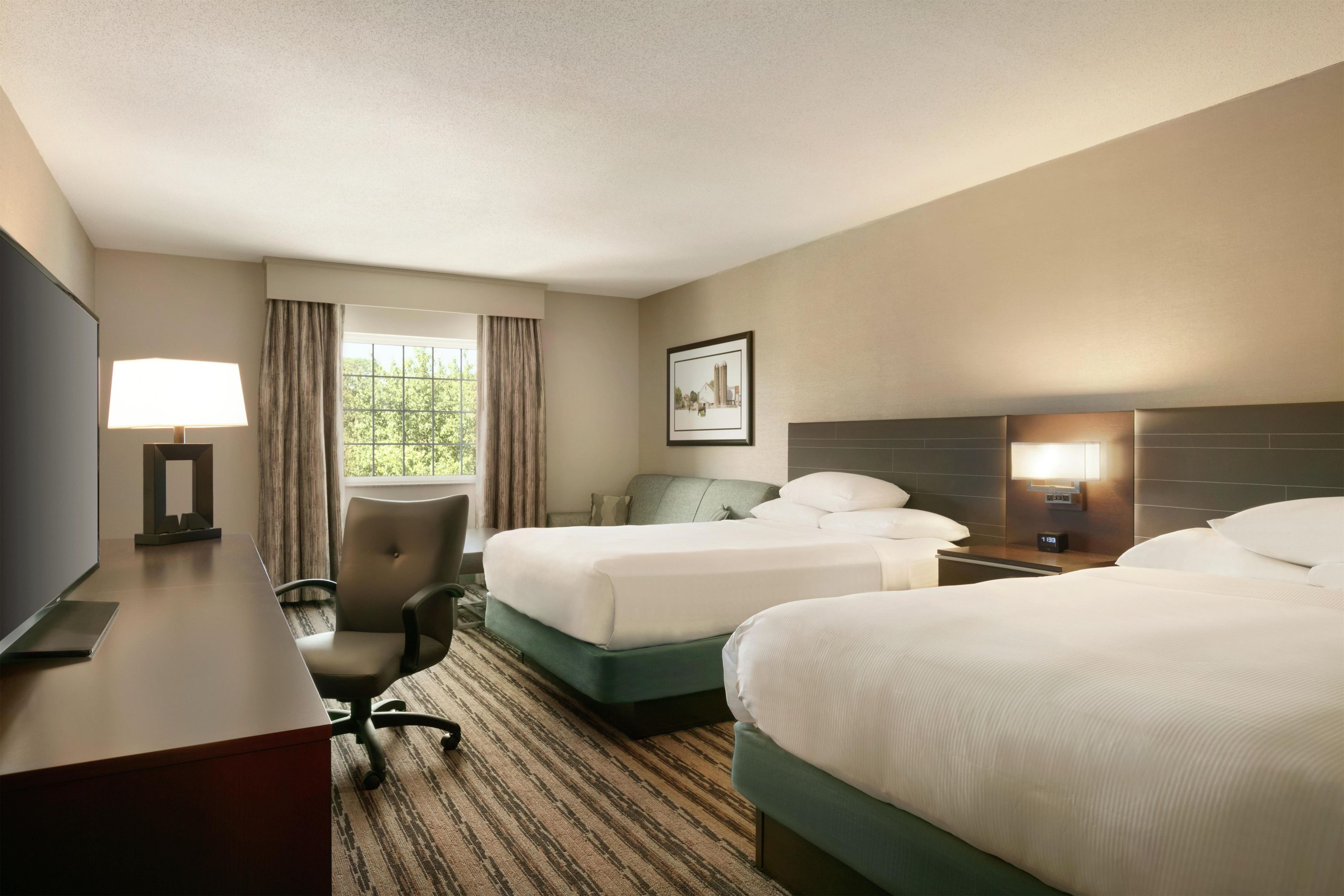 A hotel room with two beds, a desk with a lamp, a chair, and a picture on the wall.