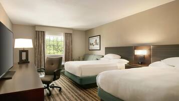 A hotel room with two beds, a desk with a lamp, a chair, and a picture on the wall.