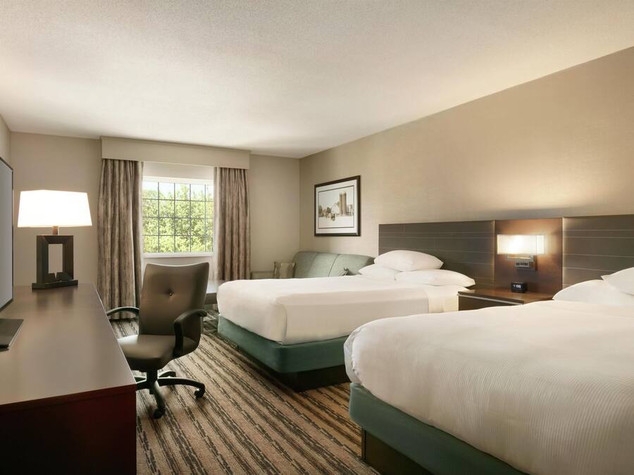 A hotel room with two beds, a desk with a lamp, a chair, and a picture on the wall.