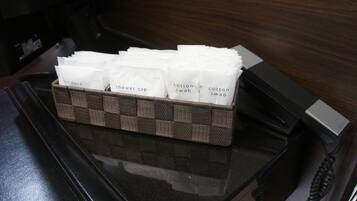 A black telephone with a brown woven basket containing white paper towels labeled with various amenities like 'air band', 'shower cap', and 'cotton swab'.
