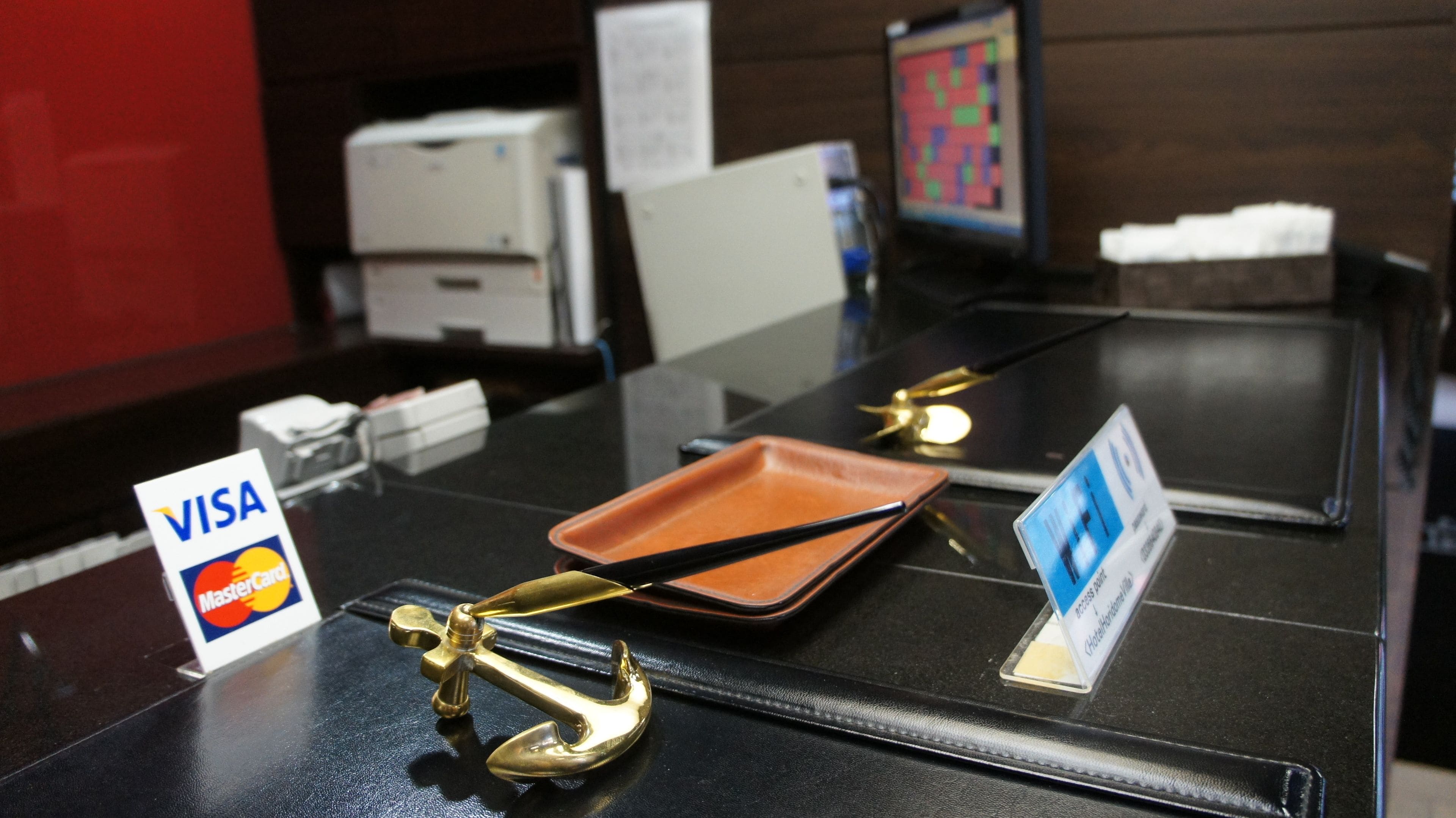 A reception desk with a black surface, a brass door handle, a VISA sign, and a MasterCard sign.