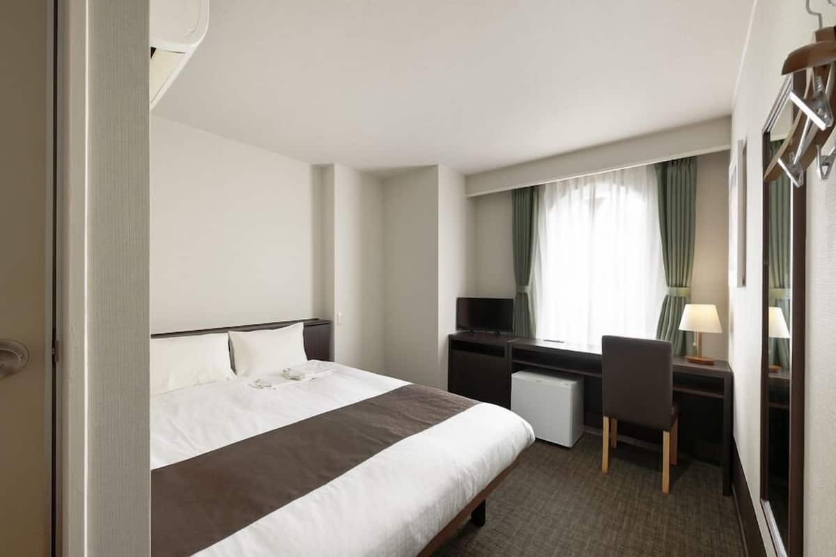 A hotel room with a bed, desk, chair, TV, and a window with curtains.