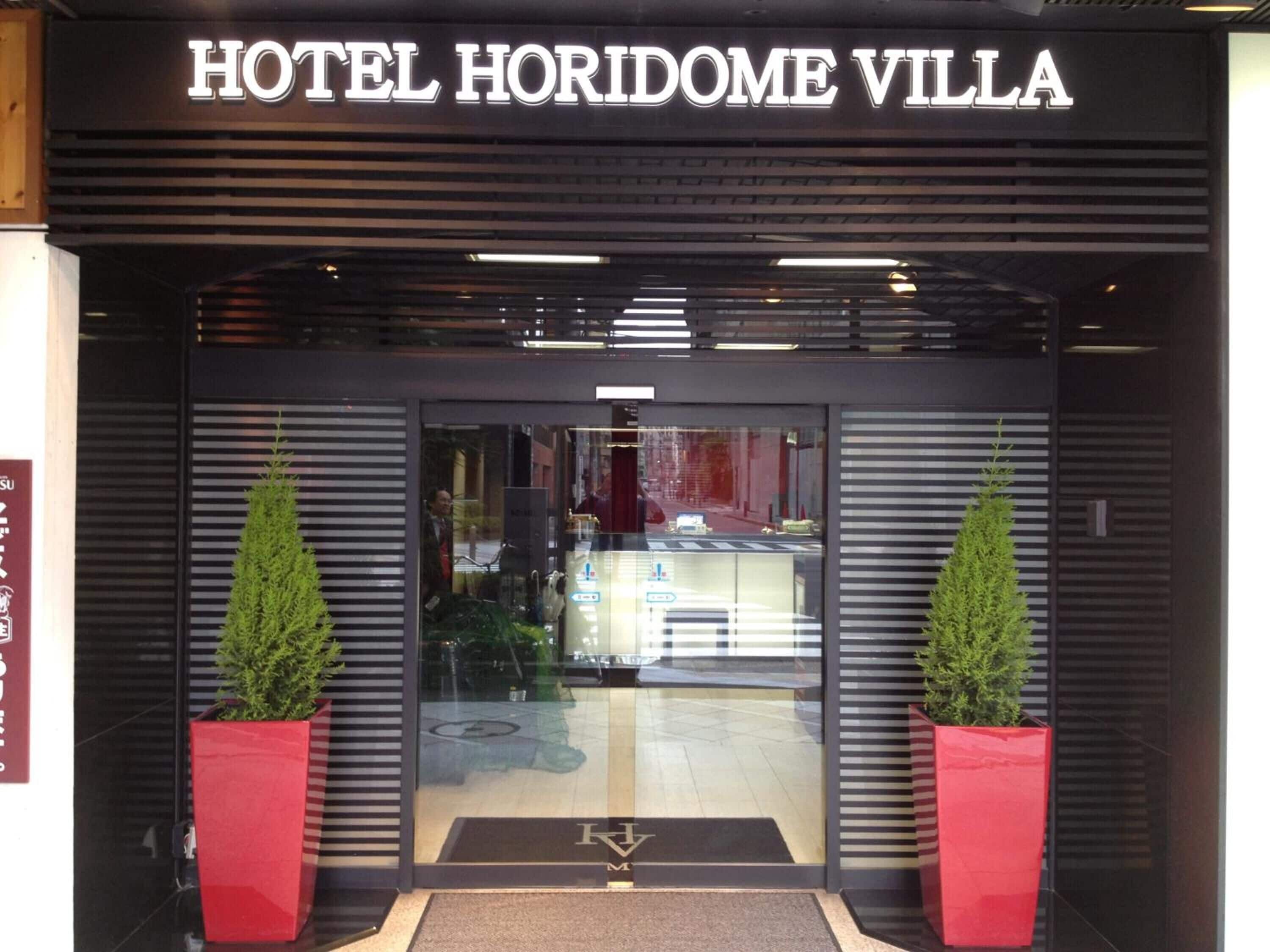 The entrance to HOTEL HORIZOME VILLA with a modern design, featuring two potted plants on either side of the entrance.