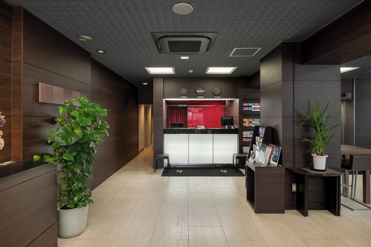 A reception area with a reception desk, a large potted plant, a red curtain, and a clock on the wall.
