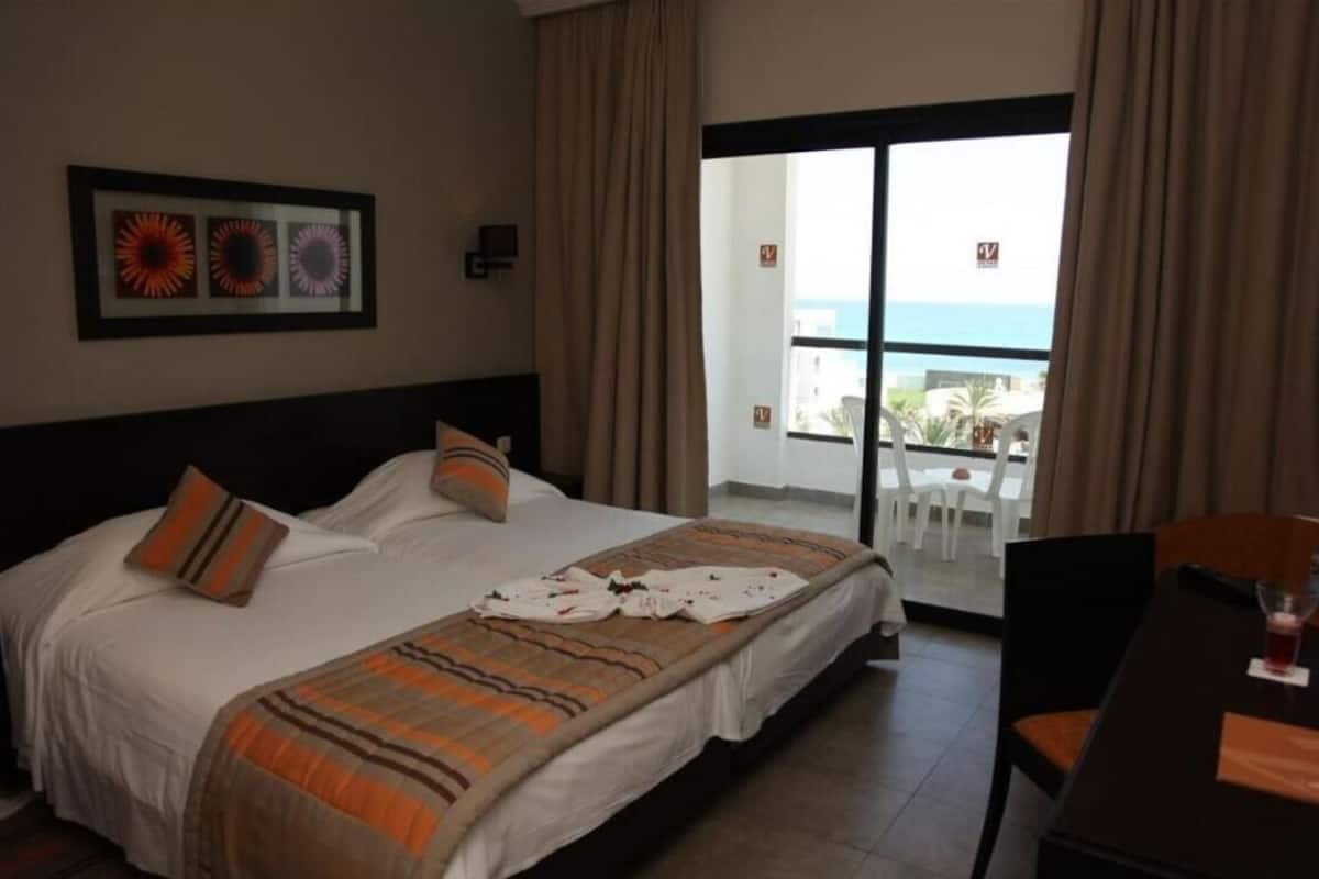A hotel room with a bed, a dining table, and a view of the ocean.