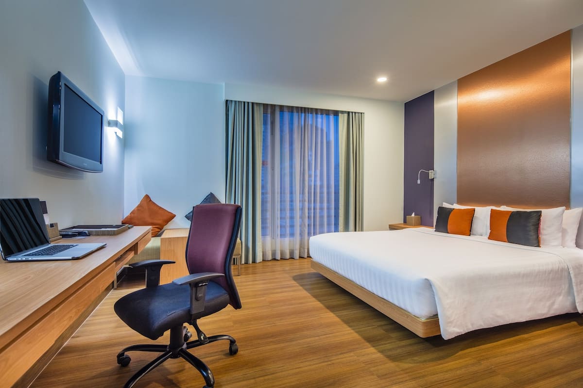 A hotel room with a bed, desk, chair, and a TV on the wall.