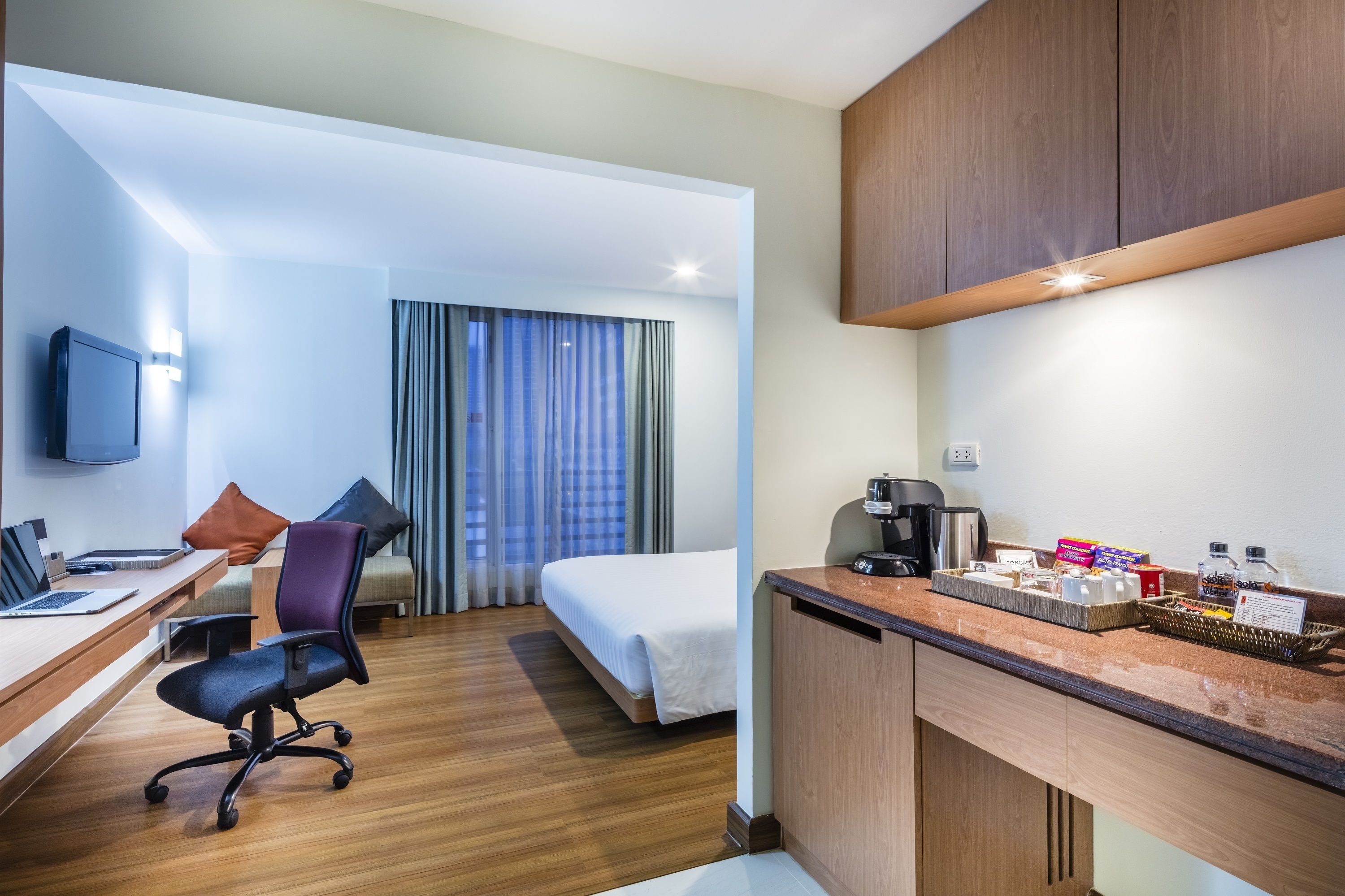 A hotel room with a bed, desk, chair, and kitchenette.