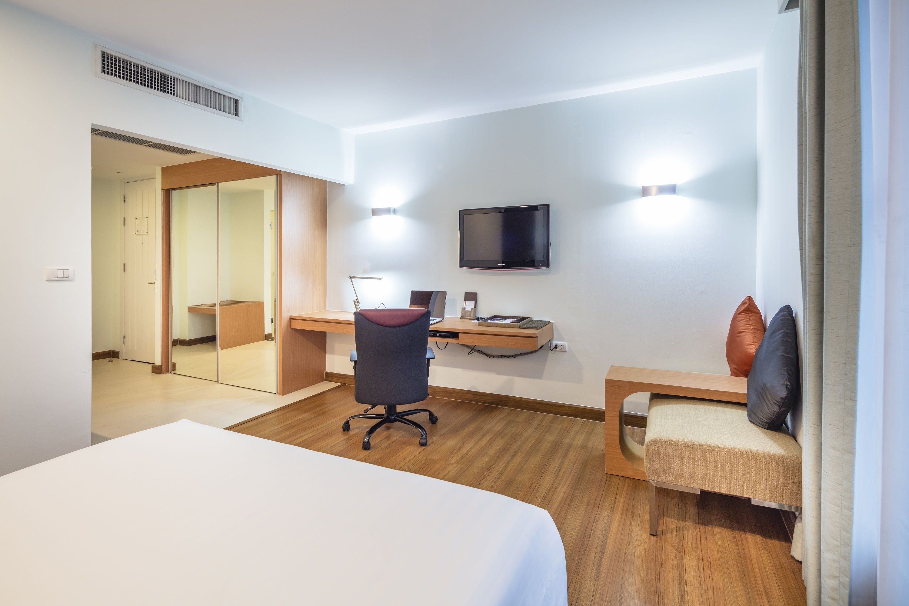 A hotel room with a bed, desk, chair, TV, and a mirror.