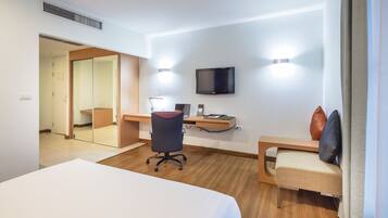 A hotel room with a bed, desk, chair, TV, and a mirror.