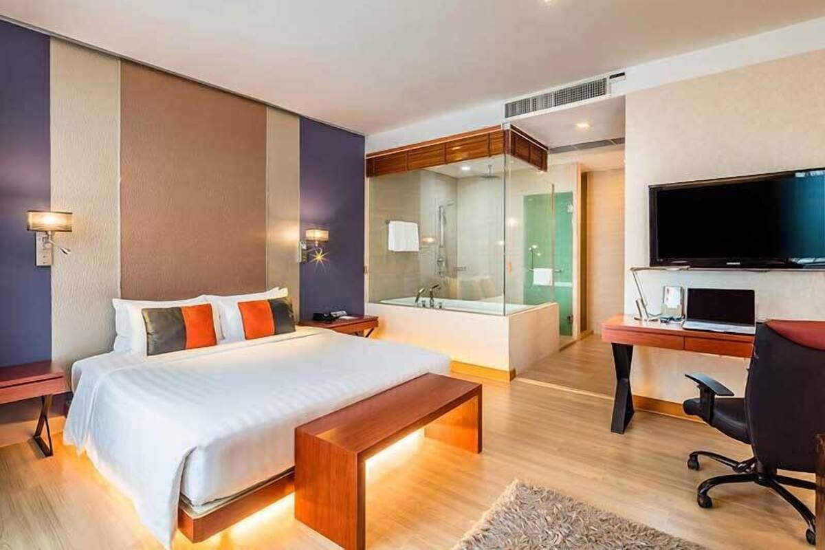 Une chambre d’hôtel moderne dotée d’un grand lit, d’un bureau avec un ordinateur, d’une télévision et d’une douche séparée par des parois en verre.