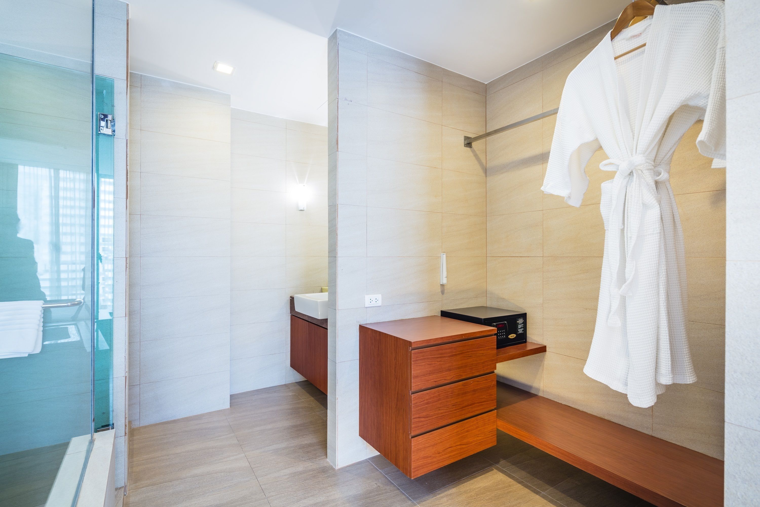 A modern bathroom with a glass shower enclosure, a wooden vanity with a sink, and a robe hanging on a towel rack.