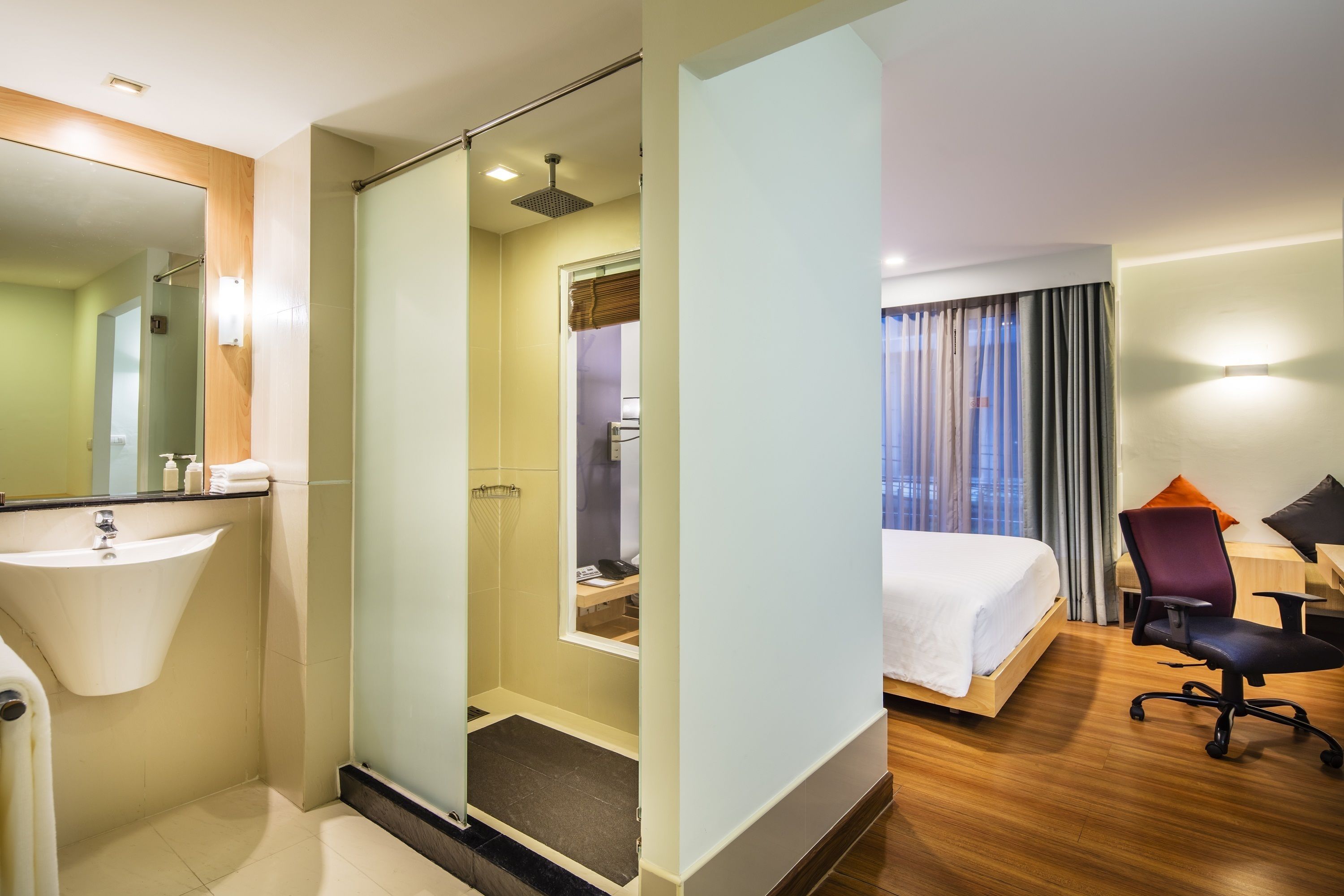 A hotel room with a bathroom, a bed, a desk, and a chair.