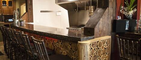A bar area with a long counter, multiple stools, and a wooden log wall.
