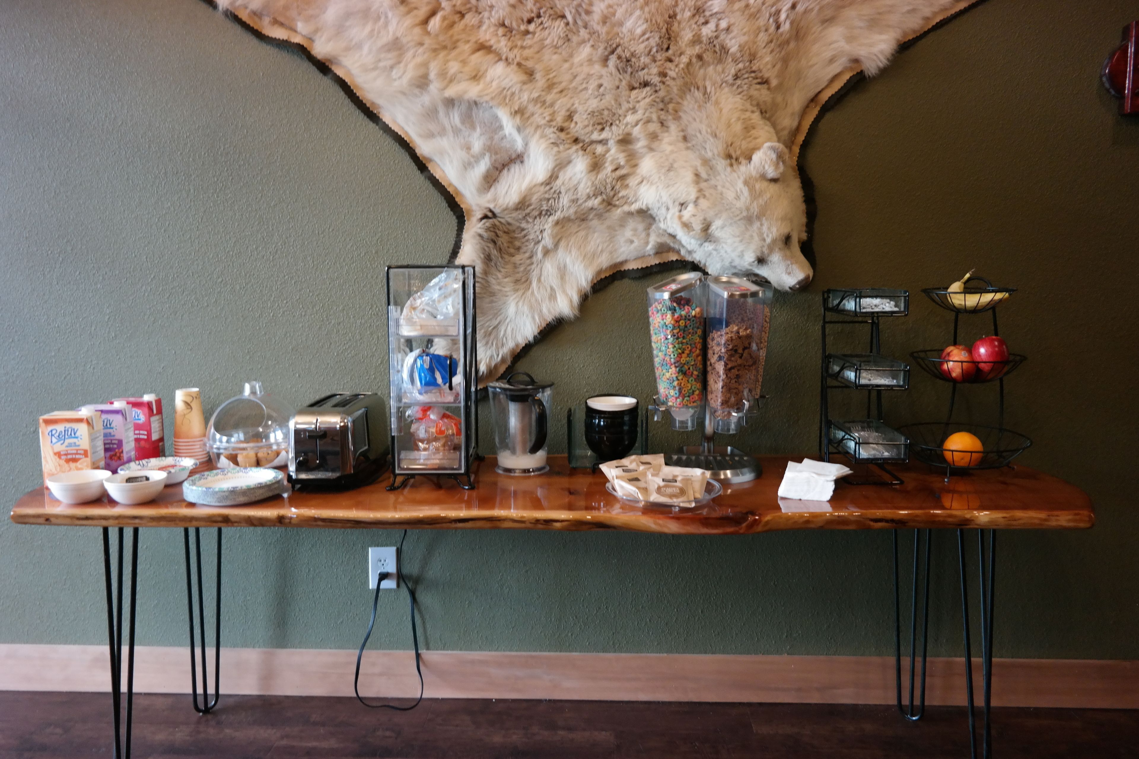 Une table en bois sur laquelle sont disposés divers aliments pour le petit-déjeuner, une machine à café, ainsi qu’une variété de fruits et de collations.